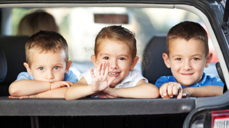 Three children and mother in the car looking and waving their hands, as if saying goodbye to somebody while traveling for a vacation. Selective Focus, focus is on the girl